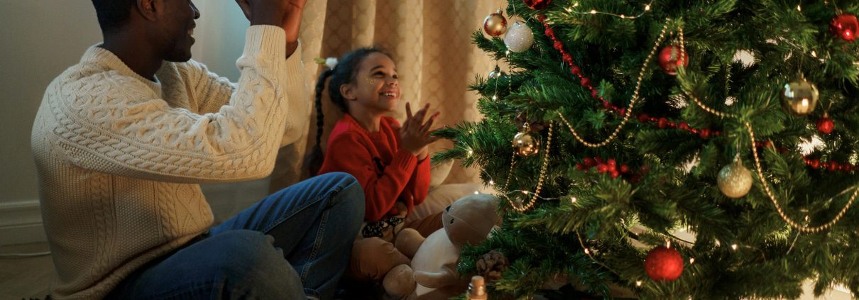 a father and a daughter sitting around a christmas tree with presents under it