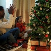 a father and a daughter sitting around a christmas tree with presents under it