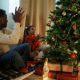 a father and a daughter sitting around a christmas tree with presents under it